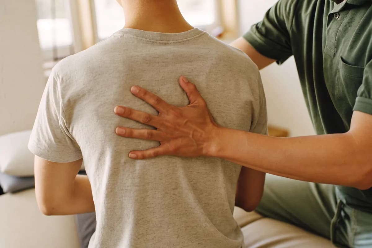 Therapeutenhand liegt ruhig auf dem Rücken eines bekleideten Patienten